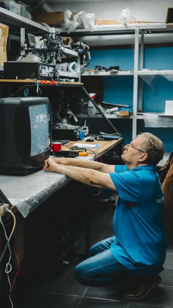 services-03 Man repairing an old television with static in a cluttered workshop setting.