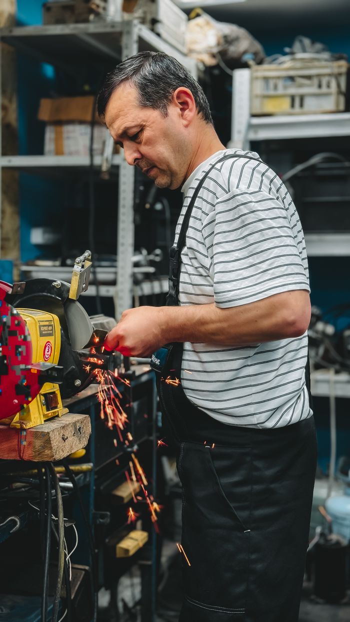 services-01 Focused man using a grinder machine with sparks flying in a workshop setting.