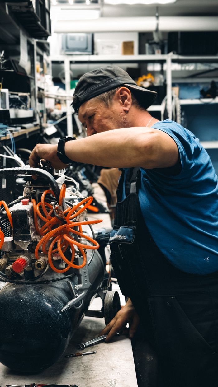 services-04 Skilled mechanic repairing air compressor in a cluttered workshop setting.